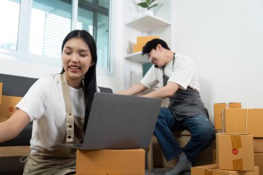 Bir çift, dizüstü bilgisayar üzerinde çalışırken ve paketleri taşırken, bir iş ortamında ortaklıklarını sergiledikleri bir anı paylaşıyor..