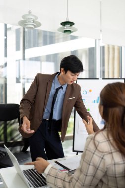 Bir iş adamı, modern ofis alanındaki bir toplantıda bir meslektaşıyla proje stratejilerini tartışırken el kol hareketi yapar..