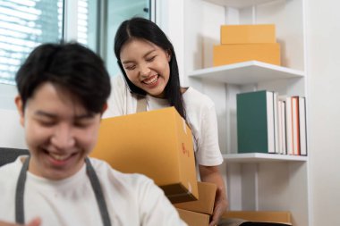 Paketleri yönetirken ve bir dizüstü bilgisayarla iş birliği yaparken gülümseyen bir çift. İş ortamında ortaklıklarını gösteriyorlar..