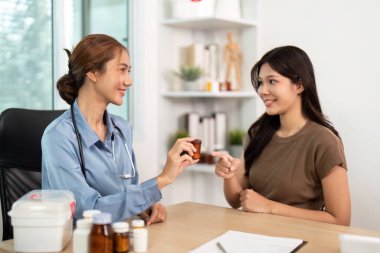 Bir hemşire bir hastaya ilaç şişesi verir, tıbbi bir ortamda tedavi ve iletişim gösterir..