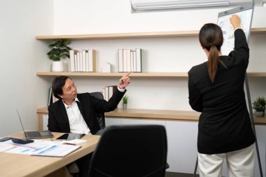 Erkek bir danışman, toplantı odasında kadın bir meslektaşla mali ölçümleri tartışırken bir tabloya işaret eder..