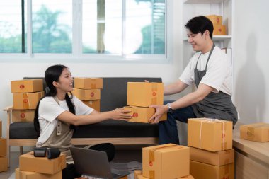 Konforlu bir ev ofisinde, bir partner, takım çalışmasını ve bağlantıyı vurgulayarak, bir kutuyu diğerine uzatırken, bir çift iş birliği yapar..