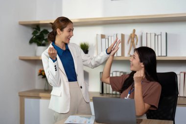 İki kadın birlikte çalışırken keyifli bir anı paylaşıyorlar. Pozitif ve işbirlikçi bir ofis atmosferini somutlaştırıyorlar..