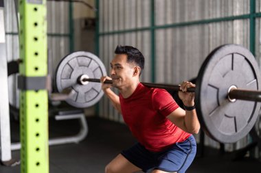 Odaklanmış bir erkek sporcu, spor salonunda dayanıklılık eğitimine adanmışlığını göstererek ağır sıkletlerle çömeliyor..