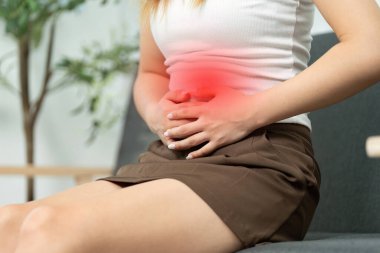 Genç bir kadın kanepede oturup, karnını ağrıtarak, karın rahatsızlığını vurguluyor..