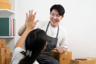 Kutular ve dizüstü bilgisayarlarla çevrili küçük bir işletmeyi yönetirken birlikte eğlenen bir çift, takım çalışması ve mutluluk sergiliyor..