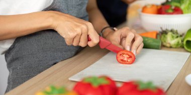 Bir çift birlikte yemek yapmayı, domates doğramayı ve taze malzemelerle dolu canlı bir mutfakta gülümsemeyi seviyor..