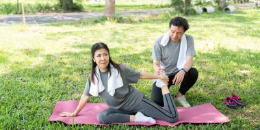 Bir çift parkta eşli yoga yapıyor, esnekliği ve duygusal bağlantıyı geliştiriyor..