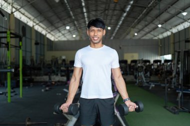 Kararlı bir genç adam, iyi donanımlı bir spor salonunda dambıllarla güç antrenmanı yapar..