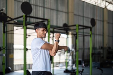 Genç bir adam spor salonundaki antrenmandan sonra esneme hareketleri yapar. Gücün, esnekliğin ve sağlığın düzelmesinin altını çizer..