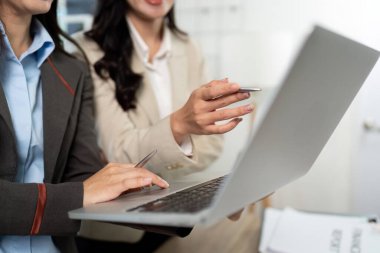 İş kıyafeti giymiş iki kadın bir dizüstü bilgisayar üzerinde işbirliği yapıyor, modern ofis ortamında anlayış ve stratejilerini paylaşıyorlar..