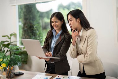 Bir dizüstü bilgisayarda veri analiz eden iki kadın, profesyonel bir ortamda takım çalışması ve stratejik planlama sergiliyor..