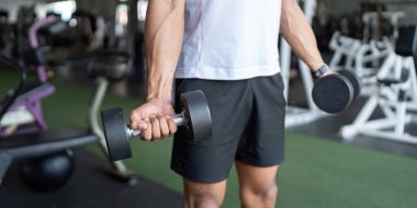Bir erkek spor salonunda güç antrenmanı ve forma odaklanarak dambıl egzersizi yapar..