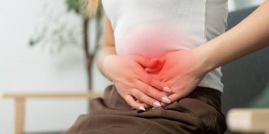 Karnını tutan genç bir kadın karın ağrısına işaret ediyor. Bu görüntü, sağlık belirtilerini tanımanın önemini vurgular..