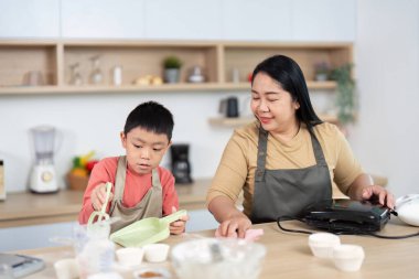 Bir anne ve oğlu sıcak bir mutfakta temizlik ve pişirme malzemelerini hazırlarken keyifli bir anı paylaşıyorlar..