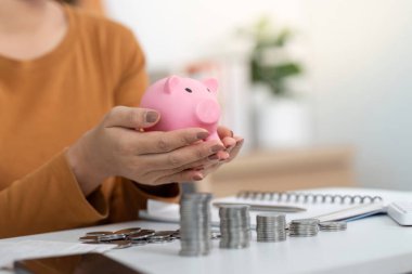 Etrafı bozuk paralarla çevrili pembe bir kumbarayı beşikte tutmak gelecekteki finansal hedefler için tasarruf kavramını gözler önüne seriyor..