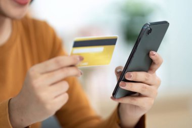 Genç bir kadın, akıllı telefonuna dijital ödeme yaparken elinde bir kredi kartı tutuyor. Modern finansal işlemleri ve online alışverişi gösteriyor..