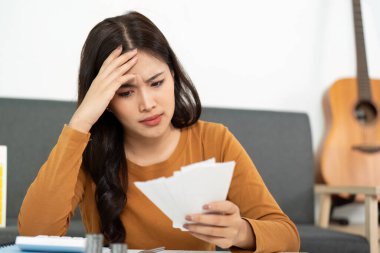 Endişeli bir kadın faturalarını endişeli bir ifadeyle inceler. Finansal stresi ve bütçeyi temsil eder..