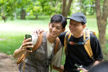 Neşeli bir baba ve oğul yürüyüş yaparken, yemyeşil ortamda selfie çekiyorlar, bağlarını ve açık hava maceralarını yansıtıyorlar..