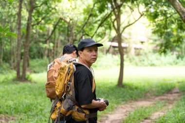 Bir baba, elinde kamerayla yürürken düşünceli bir şekilde bakar. Oğlunun da belirttiği gibi, yemyeşil ortamda ilginç bir şeye dikkat çeker..