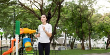 Yeşil bir parkta koşmaktan hoşlanan genç bir kadın aktif bir yaşam tarzı ve spor yapmaya olan bağlılığını somutlaştırıyor. Sağlık ve refah temaları için ideal.