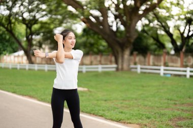 Genç bir kadın parkta dinamik bir kol hareketi yapıyor, dışarıda egzersiz yaparak sağlık ve uygunluğu teşvik ediyor..