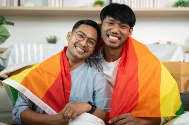 Gökkuşağı bayraklarına sarılmış, gülümseyen iki adam, sıcak bir yuva ortamında aşklarını ve kimliklerini kutluyorlar..