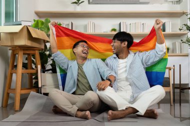 Gökkuşağı bayrağı taşıyan neşeli LGBTQIA çifti, kapalı bir ortamda gurur ve aşkı ifade ediyorlar..