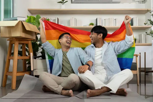 Gökkuşağı bayrağı taşıyan neşeli LGBTQIA çifti, kapalı bir ortamda gurur ve aşkı ifade ediyorlar..