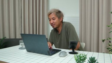 Evde oturan Asyalı bir adam, kendisine verilen bir projenin bütçesini özetlemeye odaklanmıştı. Uzaktan çalışma, sorumluluk ve konsantrasyon gösteriyordu..