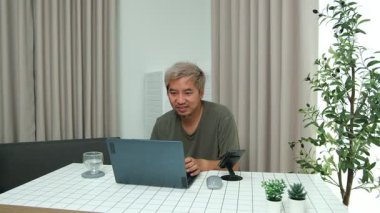 Evde oturan Asyalı bir adam, kendisine verilen bir projenin bütçesini özetlemeye odaklanmıştı. Uzaktan çalışma, sorumluluk ve konsantrasyon gösteriyordu..