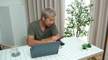 Evde oturan Asyalı bir adam, kendisine verilen bir projenin bütçesini özetlemeye odaklanmıştı. Uzaktan çalışma, sorumluluk ve konsantrasyon gösteriyordu..