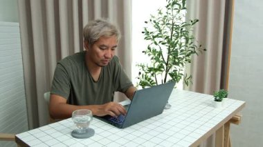 Evde oturan Asyalı bir adam, kendisine verilen bir projenin bütçesini özetlemeye odaklanmıştı. Uzaktan çalışma, sorumluluk ve konsantrasyon gösteriyordu..