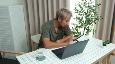 Evde oturan Asyalı bir adam, kendisine verilen bir projenin bütçesini özetlemeye odaklanmıştı. Uzaktan çalışma, sorumluluk ve konsantrasyon gösteriyordu..