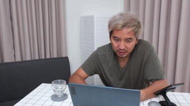 Evde oturan Asyalı bir adam, kendisine verilen bir projenin bütçesini özetlemeye odaklanmıştı. Uzaktan çalışma, sorumluluk ve konsantrasyon gösteriyordu..