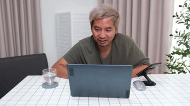 Evde oturan Asyalı bir adam, kendisine verilen bir projenin bütçesini özetlemeye odaklanmıştı. Uzaktan çalışma, sorumluluk ve konsantrasyon gösteriyordu..