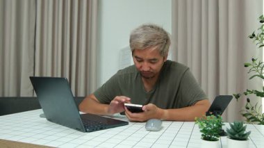 Evde oturan Asyalı bir adam, kendisine verilen bir projenin bütçesini özetlemeye odaklanmıştı. Uzaktan çalışma, sorumluluk ve konsantrasyon gösteriyordu..