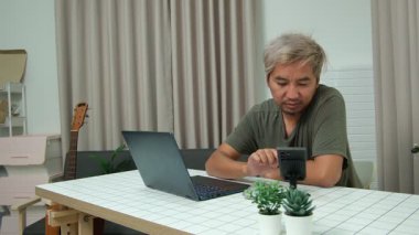 Evde oturan Asyalı bir adam, kendisine verilen bir projenin bütçesini özetlemeye odaklanmıştı. Uzaktan çalışma, sorumluluk ve konsantrasyon gösteriyordu..