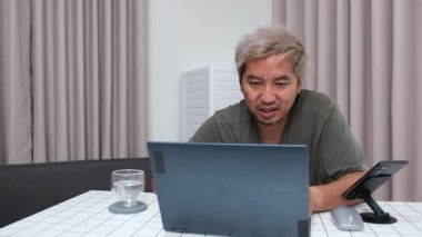 Evde oturan Asyalı bir adam, kendisine verilen bir projenin bütçesini özetlemeye odaklanmıştı. Uzaktan çalışma, sorumluluk ve konsantrasyon gösteriyordu..