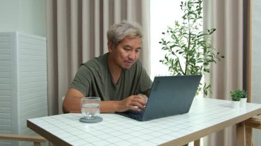 Evde oturan Asyalı bir adam, kendisine verilen bir projenin bütçesini özetlemeye odaklanmıştı. Uzaktan çalışma, sorumluluk ve konsantrasyon gösteriyordu..