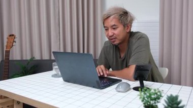 Evde oturan Asyalı bir adam, kendisine verilen bir projenin bütçesini özetlemeye odaklanmıştı. Uzaktan çalışma, sorumluluk ve konsantrasyon gösteriyordu..