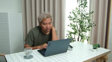 Evde oturan Asyalı bir adam, kendisine verilen bir projenin bütçesini özetlemeye odaklanmıştı. Uzaktan çalışma, sorumluluk ve konsantrasyon gösteriyordu..