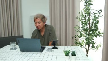 Evde oturan Asyalı bir adam, kendisine verilen bir projenin bütçesini özetlemeye odaklanmıştı. Uzaktan çalışma, sorumluluk ve konsantrasyon gösteriyordu..