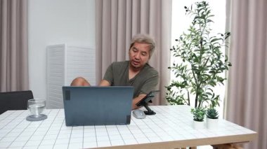 Evde oturan Asyalı bir adam, kendisine verilen bir projenin bütçesini özetlemeye odaklanmıştı. Uzaktan çalışma, sorumluluk ve konsantrasyon gösteriyordu..