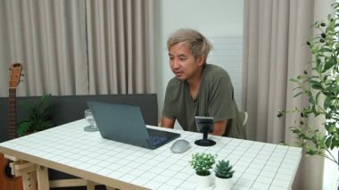 Evde oturan Asyalı bir adam, kendisine verilen bir projenin bütçesini özetlemeye odaklanmıştı. Uzaktan çalışma, sorumluluk ve konsantrasyon gösteriyordu..