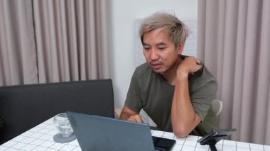 Evde oturan Asyalı bir adam, kendisine verilen bir projenin bütçesini özetlemeye odaklanmıştı. Uzaktan çalışma, sorumluluk ve konsantrasyon gösteriyordu..