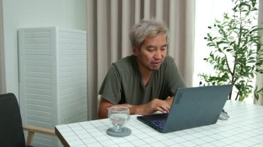 Evde oturan Asyalı bir adam, kendisine verilen bir projenin bütçesini özetlemeye odaklanmıştı. Uzaktan çalışma, sorumluluk ve konsantrasyon gösteriyordu..