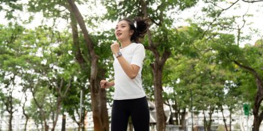 Genç bir kadın parkta koşuyor, aktif bir yaşam tarzı ve spor yapmaya kendini adamış..