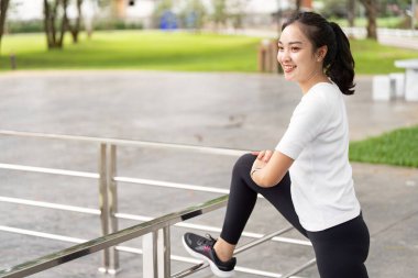 Neşeli bir kadın, bacağını korkuluklara dayar, vücut bulmuş bir spor salonu ve bir park ortamında açık hava aktivitesi..