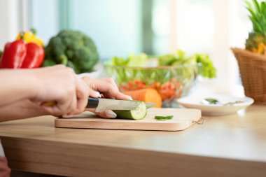 Bir kadın ustalıkla salatalığı dilimler, yemek hazırlamaya ve açık mutfak ortamında sağlıklı beslenmeye odaklanır..
